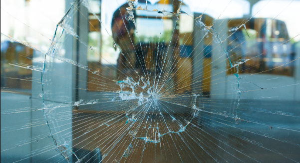Shattered glass window with a central impact point and radiating cracks; blurry outdoor reflection.