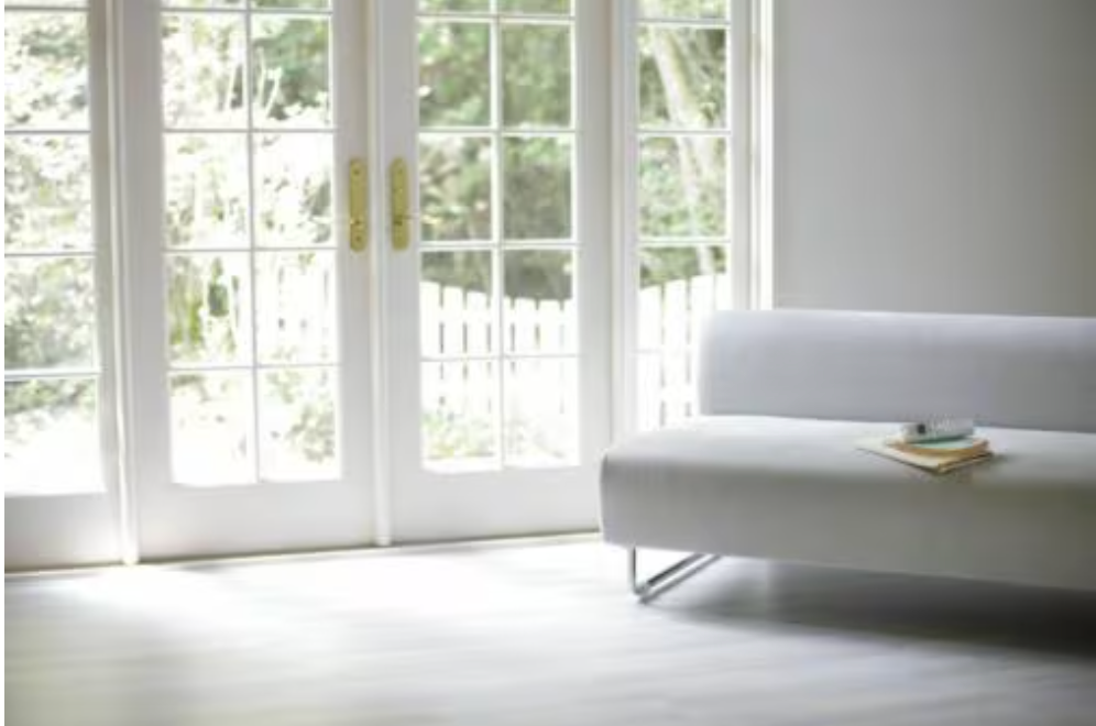 White couch in a bright room with French doors, a book rests on the seat.