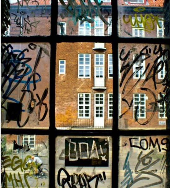 Brick building viewed through a window covered in graffiti.