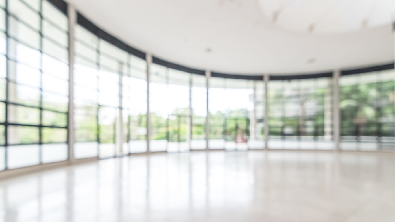 Bright, blurred, empty room with large windows, curved wall, and reflective floor.