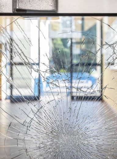 Cracked glass door; shards radiate from impact point, revealing blurred interior and doorway beyond.