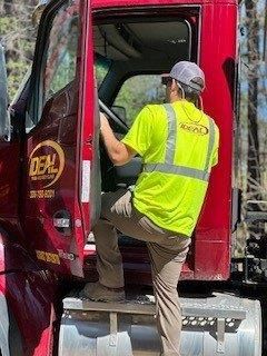 Delivery worker in neon vest climbing into a red truck cab, seen from the side.