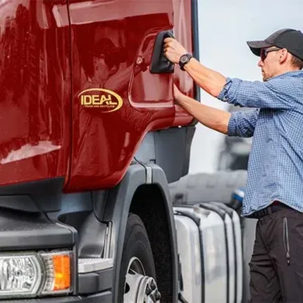Man cleaning a red semi-truck cab with a cloth outdoors