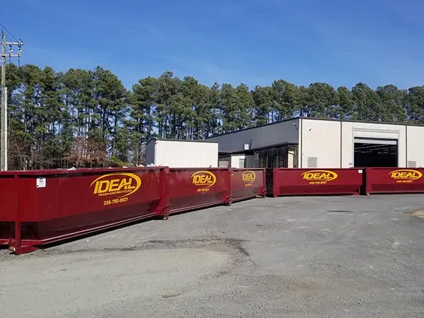 Red dumpsters outside a white building on a paved lot under a clear blue sky