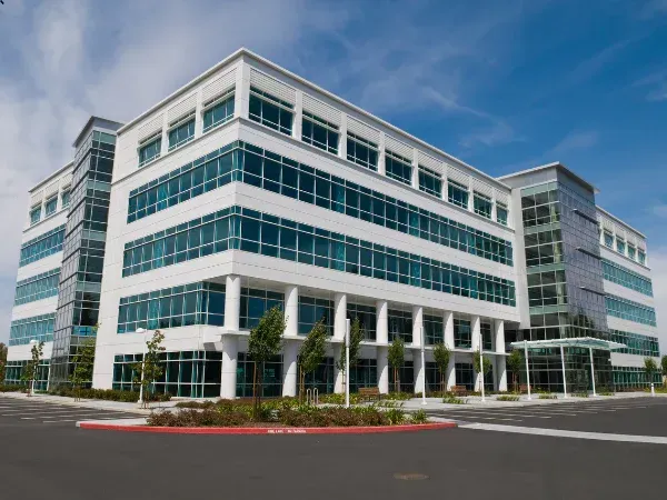 Modern white-and-glass office building with teal windows and a landscaped parking lot