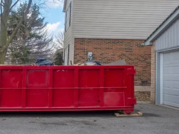 Red dumpster beside a house and garage in a driveway