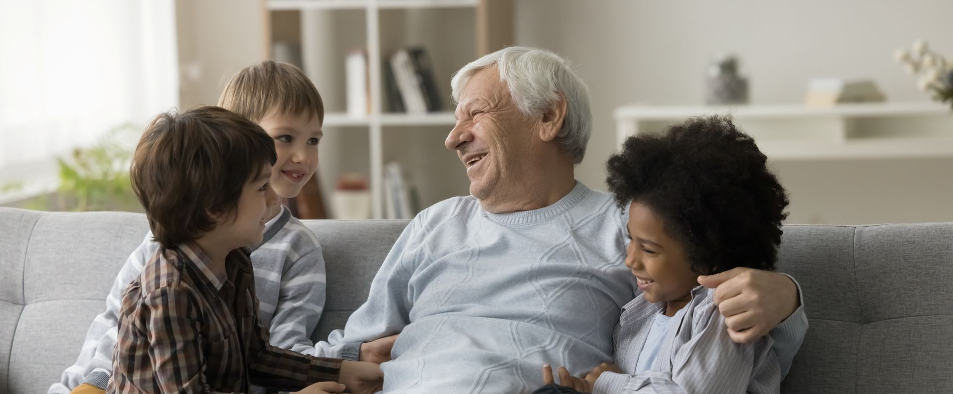An older man smiles while sitting on a couch with three children. They all are smiling and laughing.