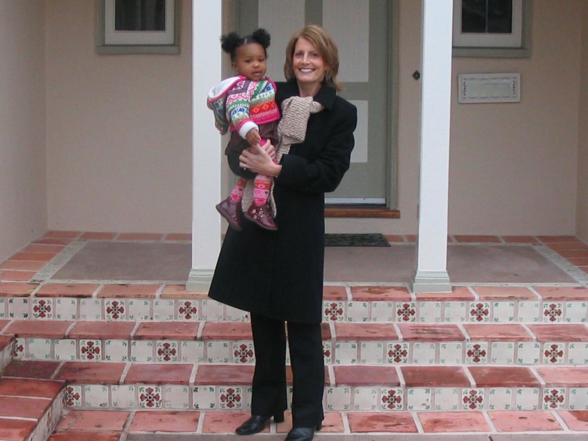 A woman in a black coat is holding a little girl in her arms