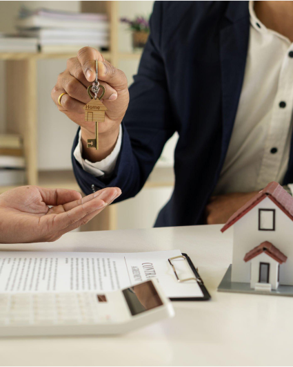 A man is handing keys to another man in front of a model house.
