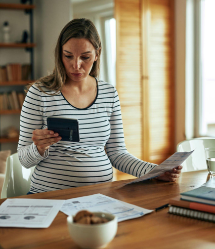 A pregnant woman is sitting at a table looking at her phone.