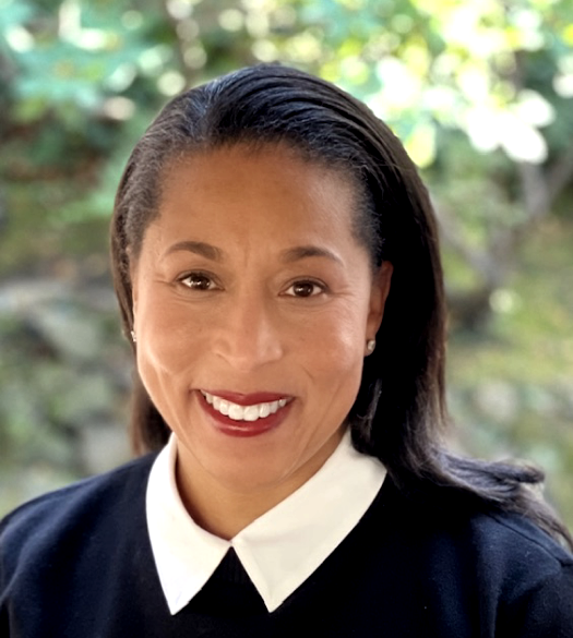 A woman wearing a black shirt with a white collar smiles for the camera