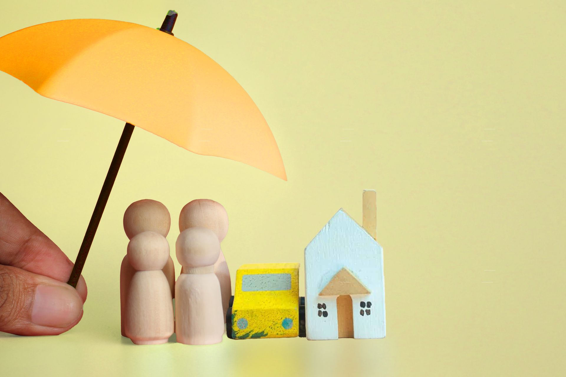 A person is holding a yellow umbrella over a couple of wooden dolls , a car , and a house.