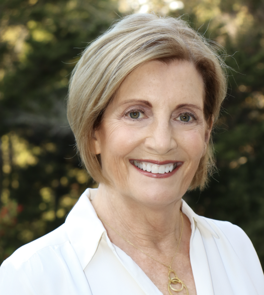 A woman wearing a white shirt and a gold necklace smiles for the camera
