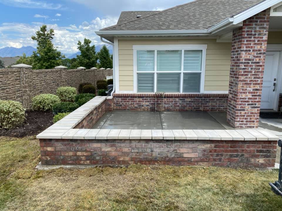 Concrete flatwork on a brick outlined patio at a yellow-sided single family home.