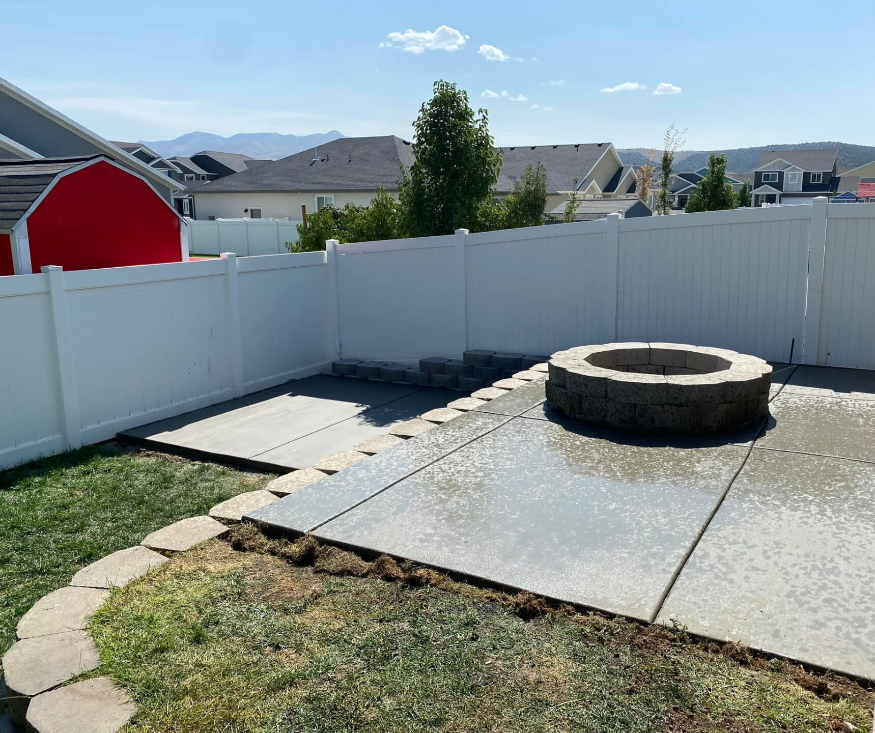 Concrete backyard patio with stone retaining wall and fireplace.