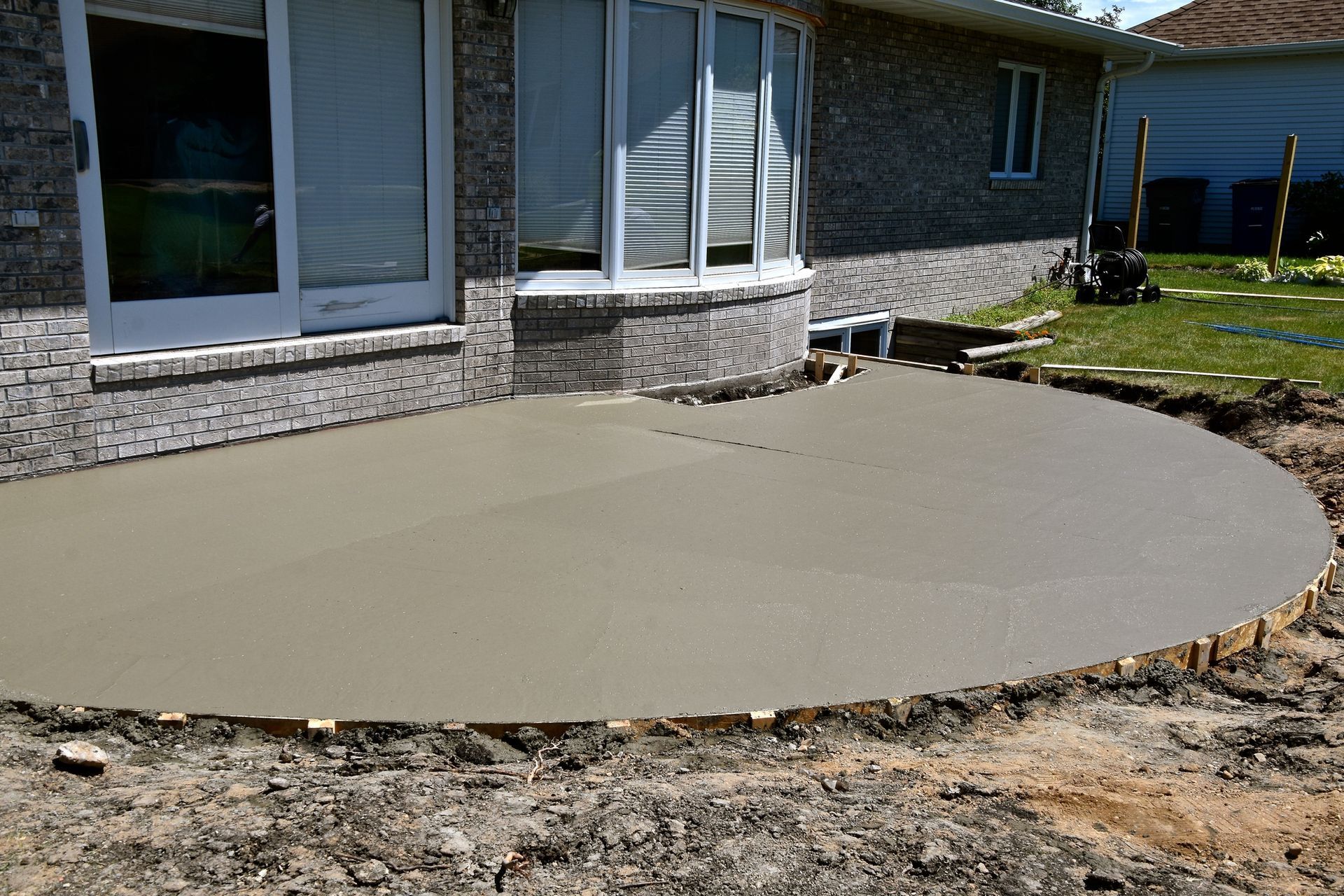 Half-circle concrete patio in the backyard of a brick single family home.