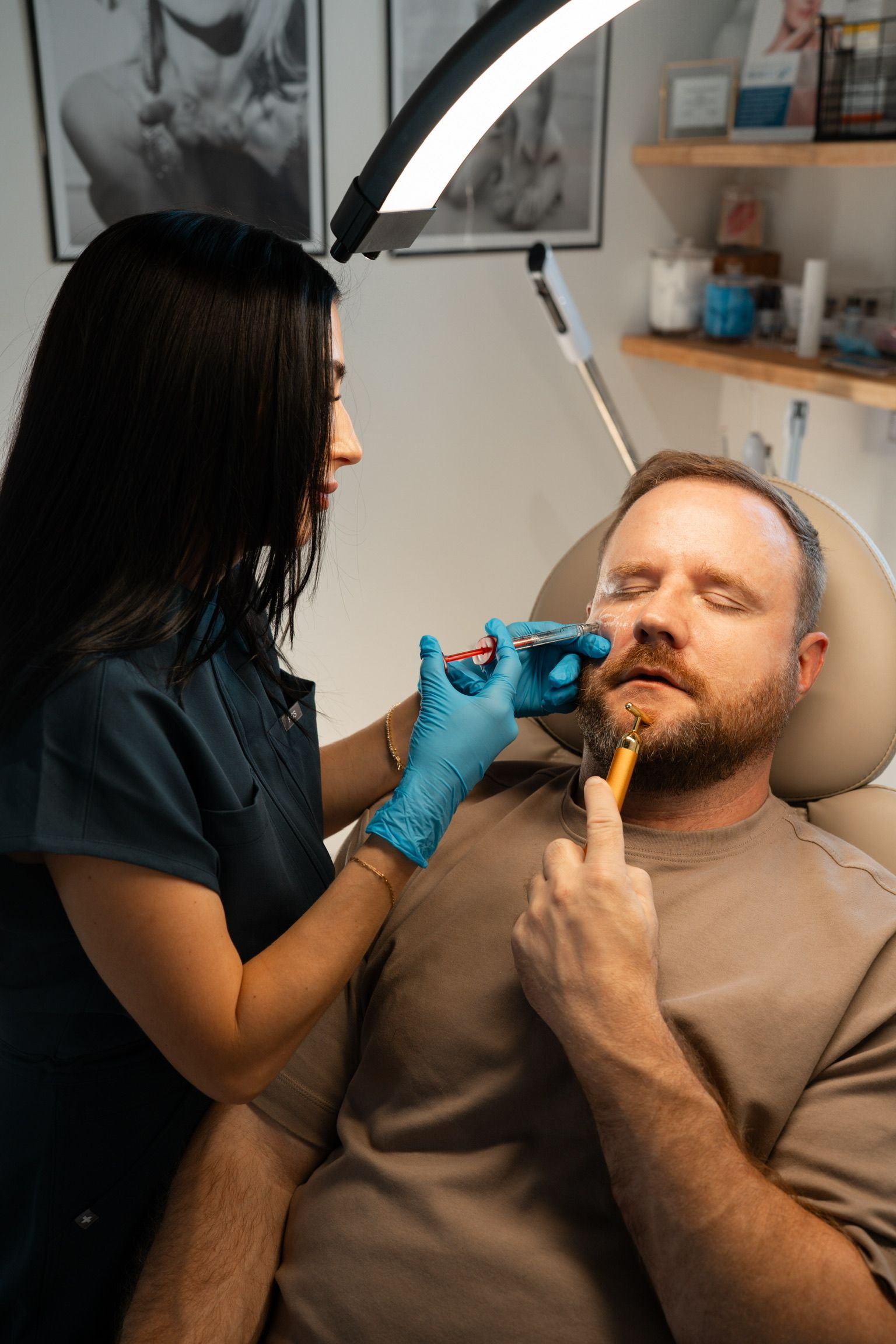 Woman in blue gloves injecting a man's face in a medical setting. The man is reclining with eyes closed.