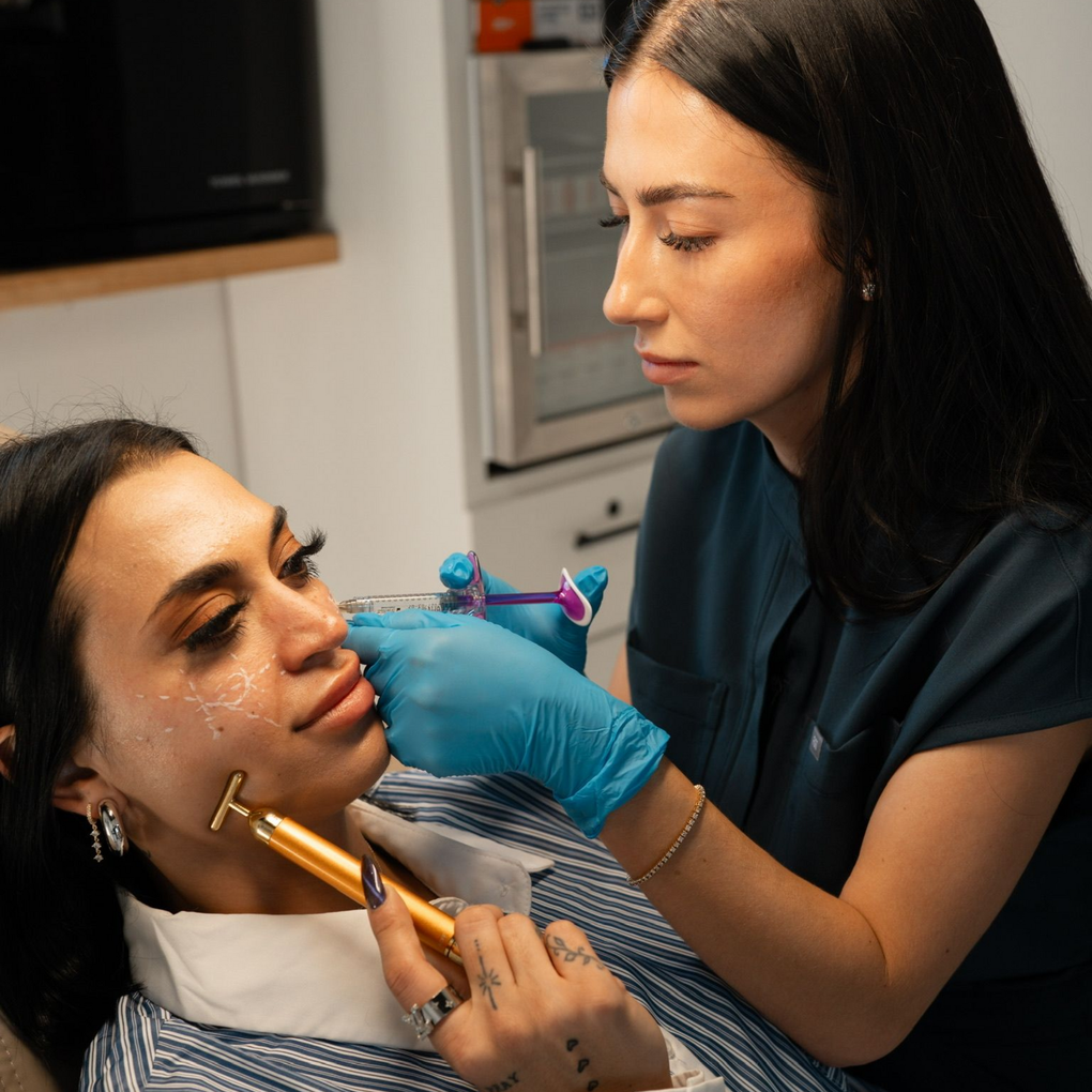 Person receiving facial treatment, with a practitioner injecting and using a needle. Indoor, clinic setting.