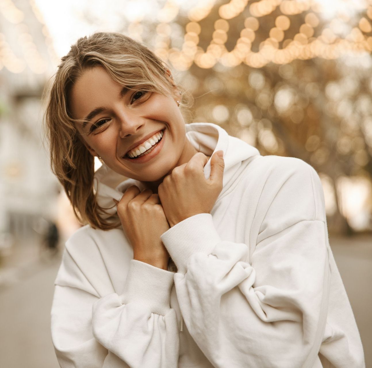 A woman in a white hoodie is smiling and looking at the camera.