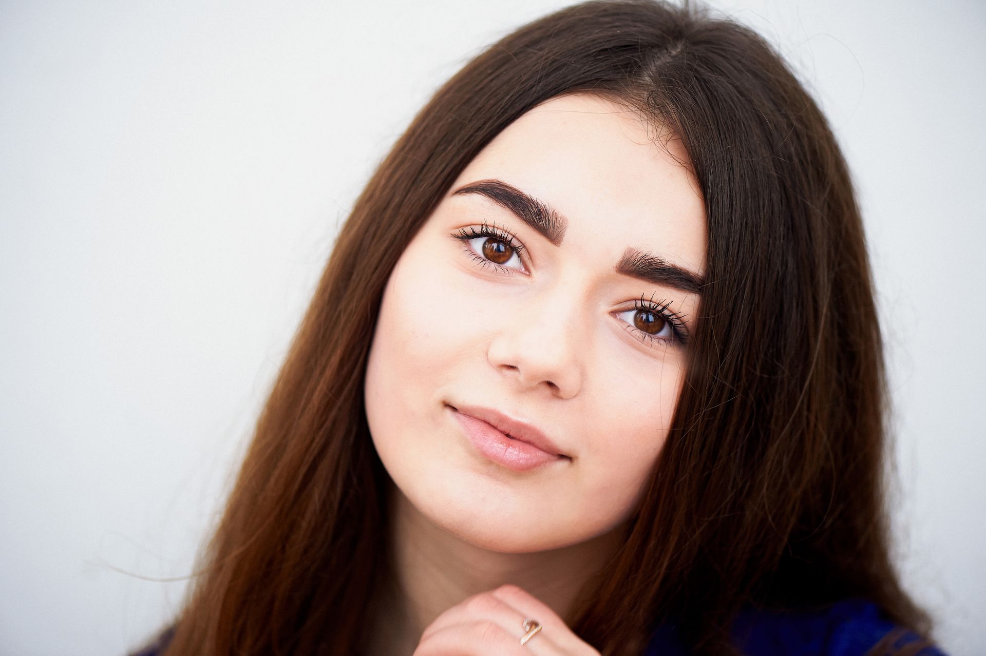 A close up of a woman 's face with long hair and a ring on her finger.