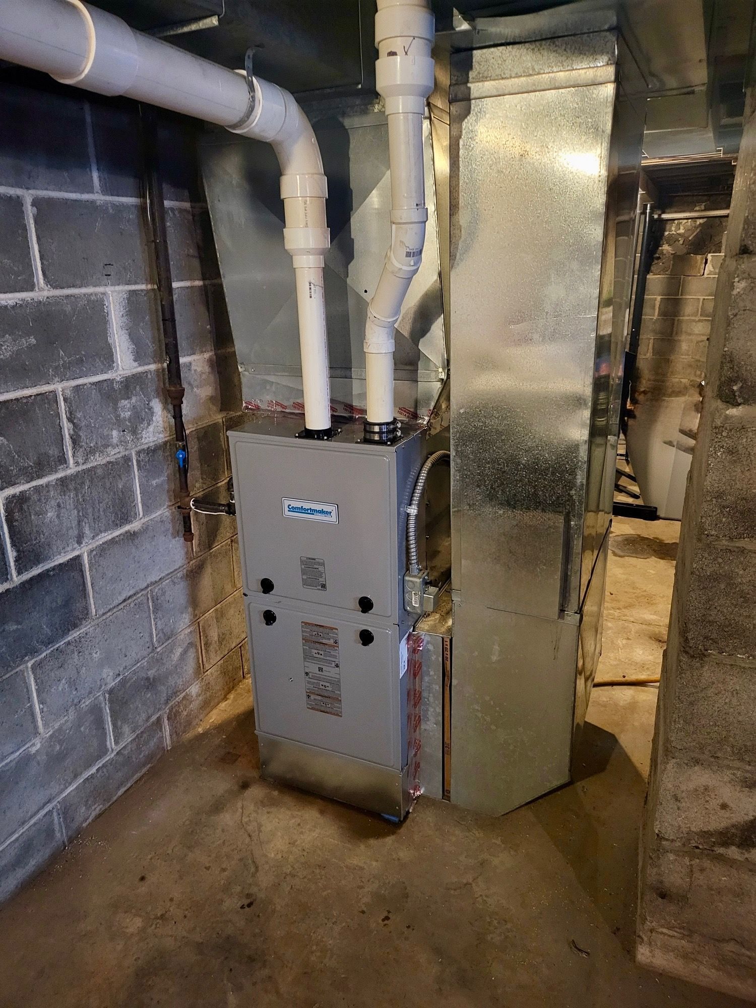 A furnace is sitting in a basement next to a brick wall.