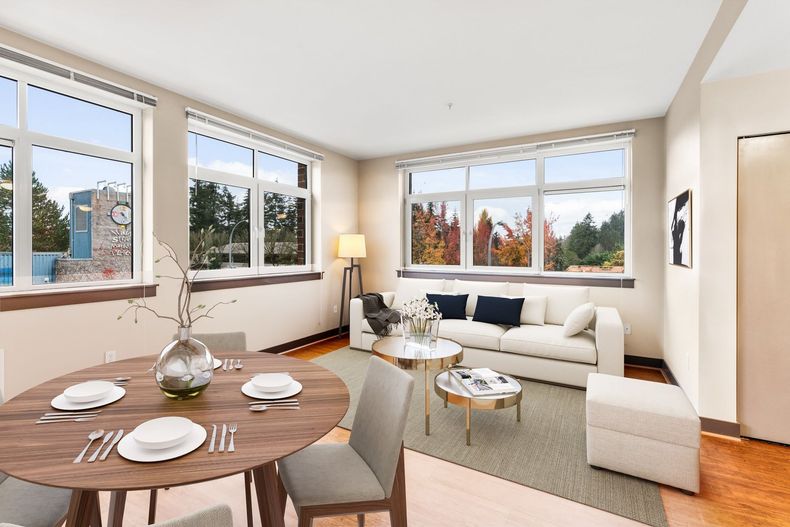 Bright living and dining room with white sofa, round table set for four, and large windows overlooking autumn trees