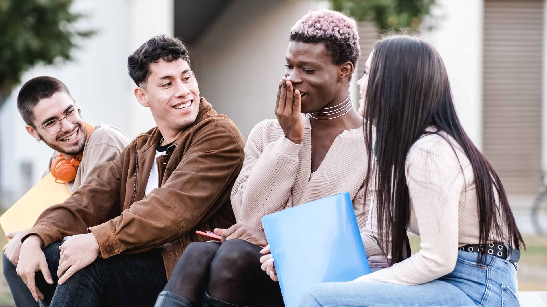 A group of young people are sitting on a bench talking to each other.