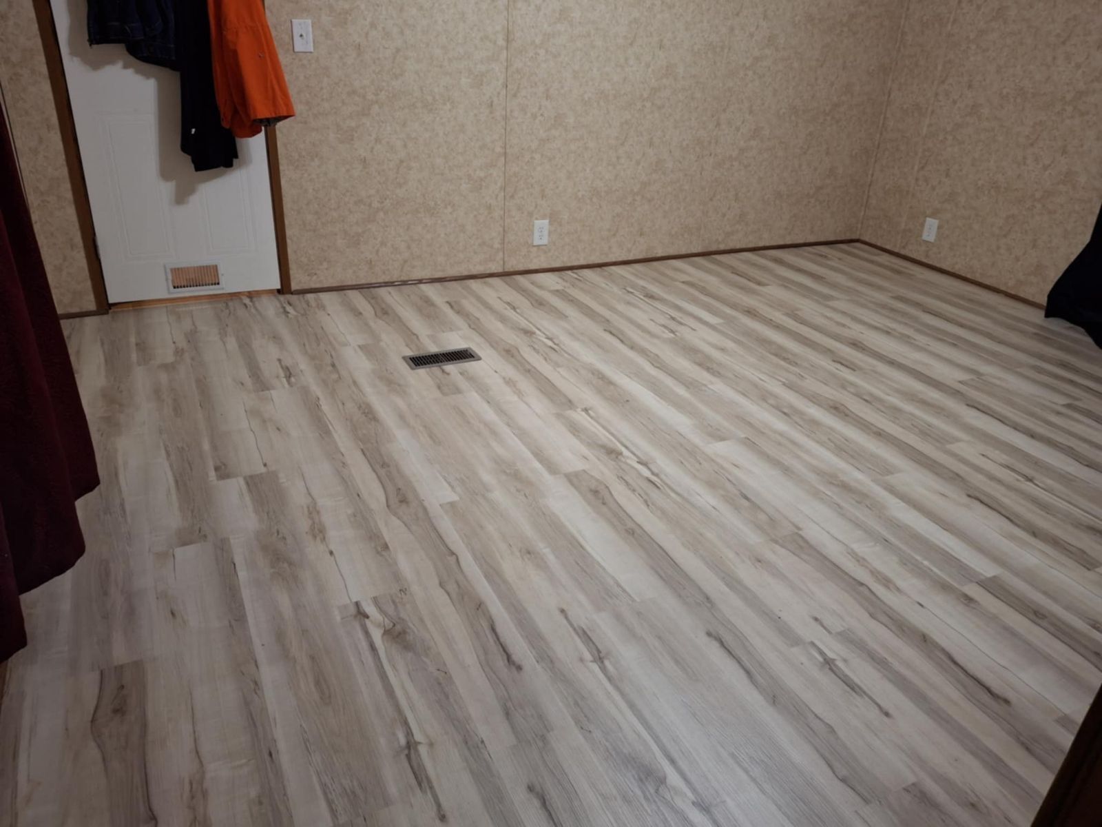 Empty room with light wood flooring, beige walls, and a floor vent near the center.