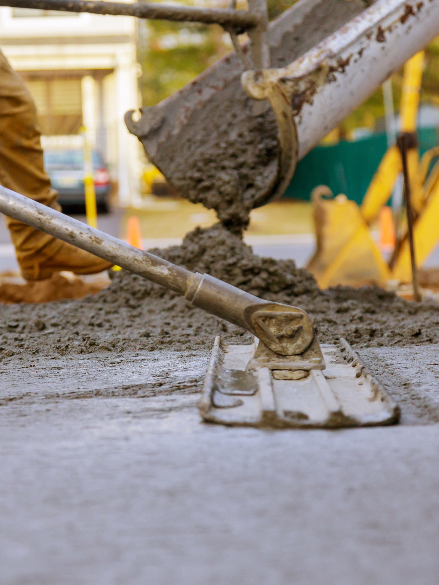 Construction workers smoothing wet concrete with a trowel and shovel at a site.