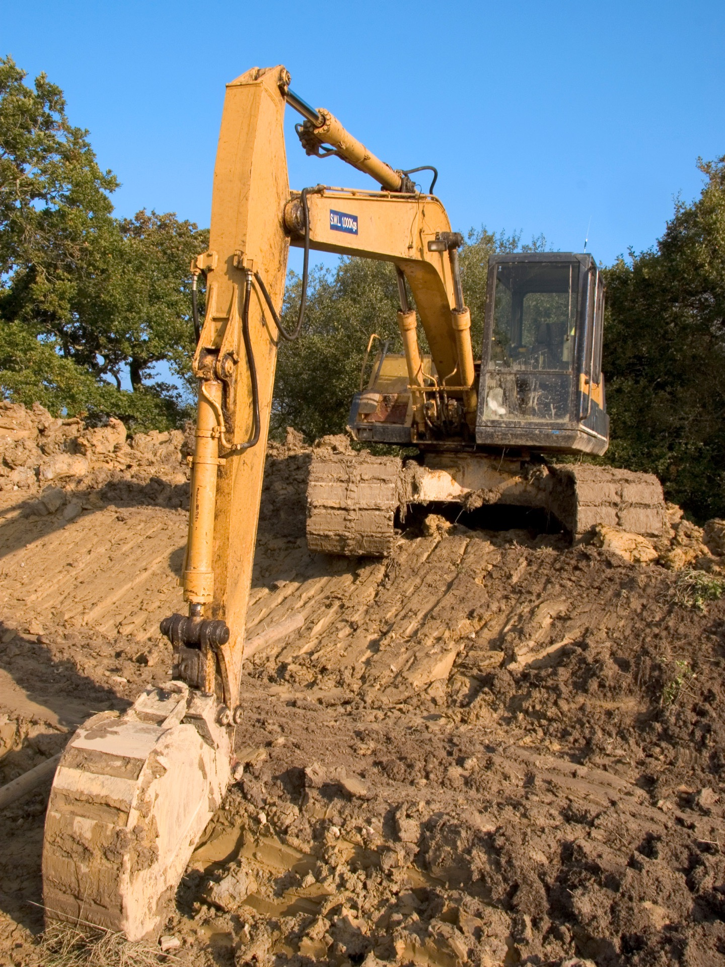 Yellow excavator digging in a dirt construction site under a clear blue sky