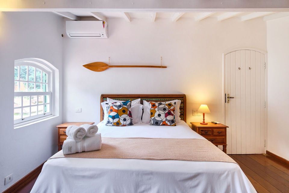 A bedroom with a bed topped with floral pillows, a wooden oar wall decor, a window, and wooden nightstands.