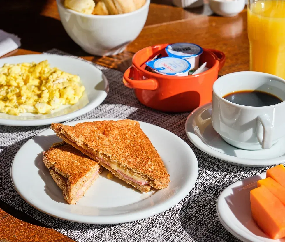 Breakfast table with toast sandwich, scrambled eggs, coffee, orange juice, and fruit cups