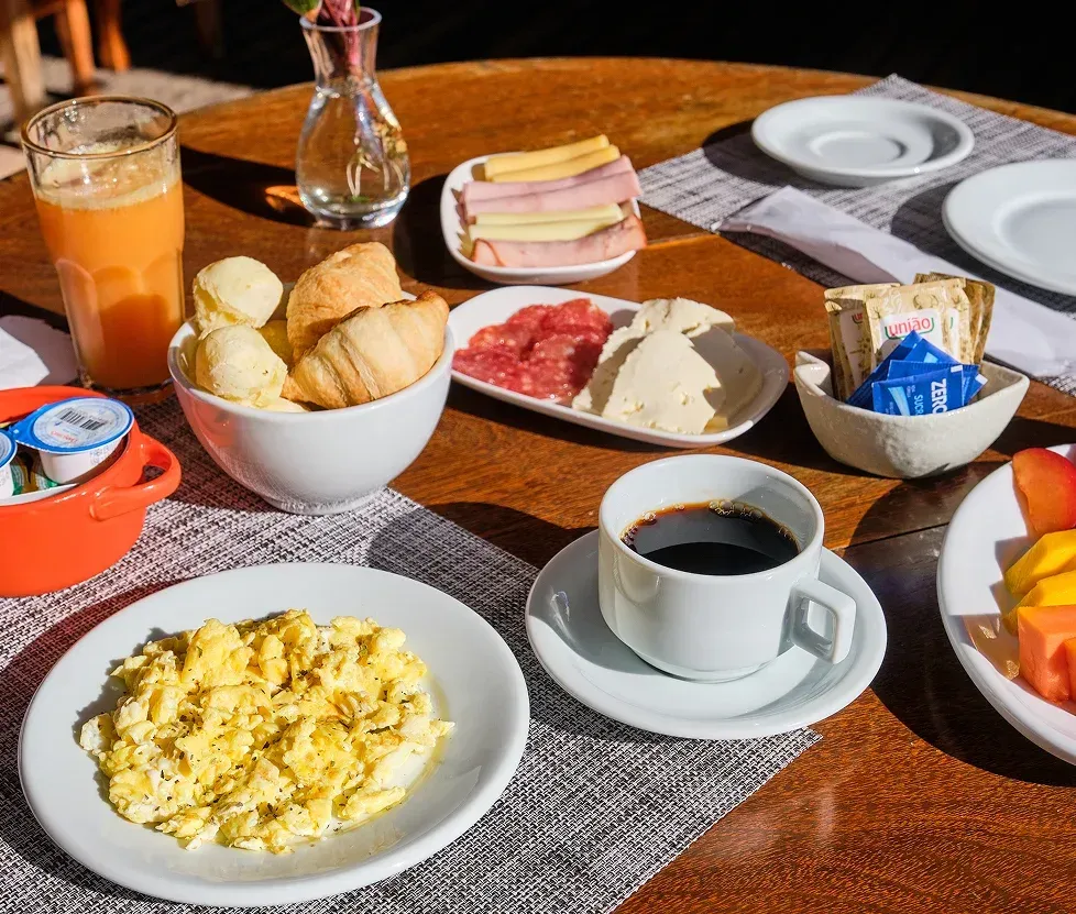 Breakfast spread with scrambled eggs, coffee, juice, bread rolls, sandwiches, and fruit on a wooden table