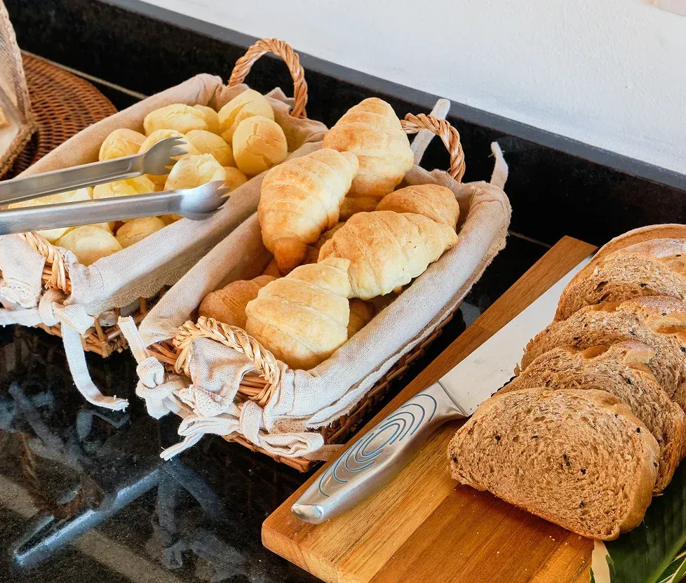 Baskets of assorted bread and rolls on a breakfast buffet table, with sliced bread on a wooden board.