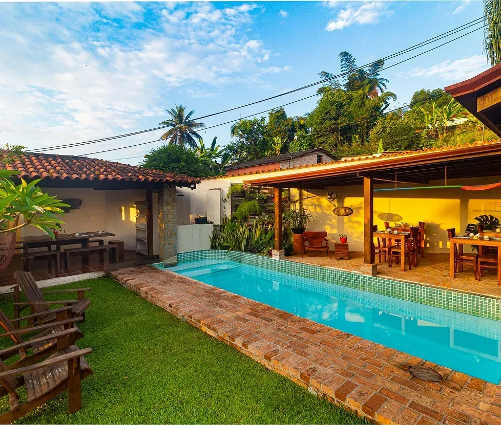 Backyard patio with a turquoise pool beside a warmly lit open-air dining area at dusk