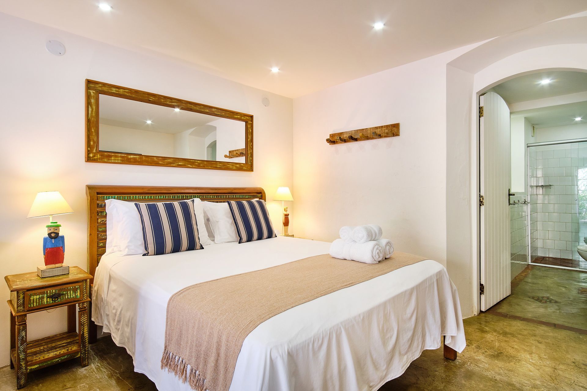 Bright bedroom with a king bed, striped pillows, bedside lamps, and an open bathroom doorway.