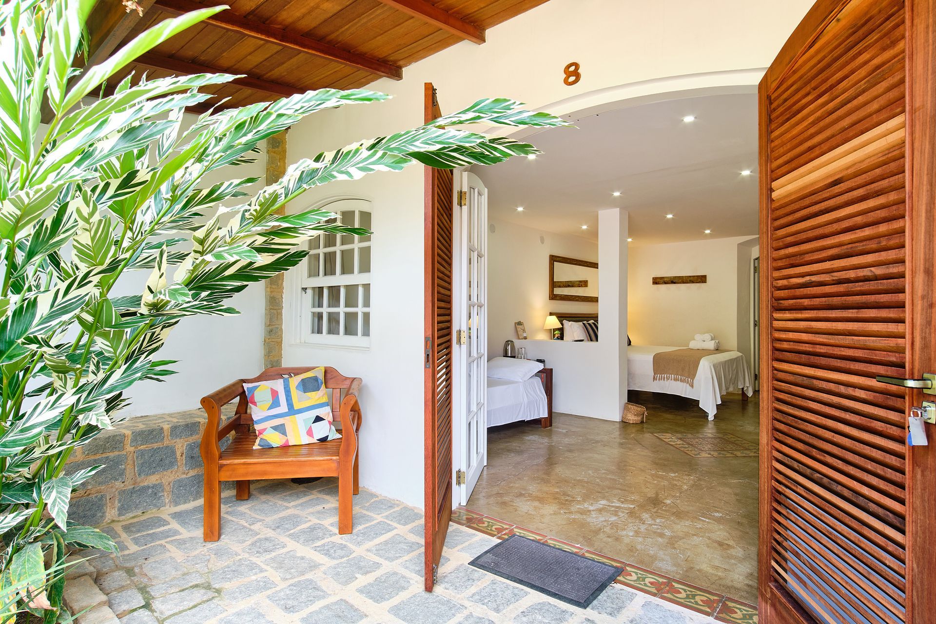 A wooden chair sits on a stone patio outside a room doorway, labeled number 8, with a bedroom visible inside.