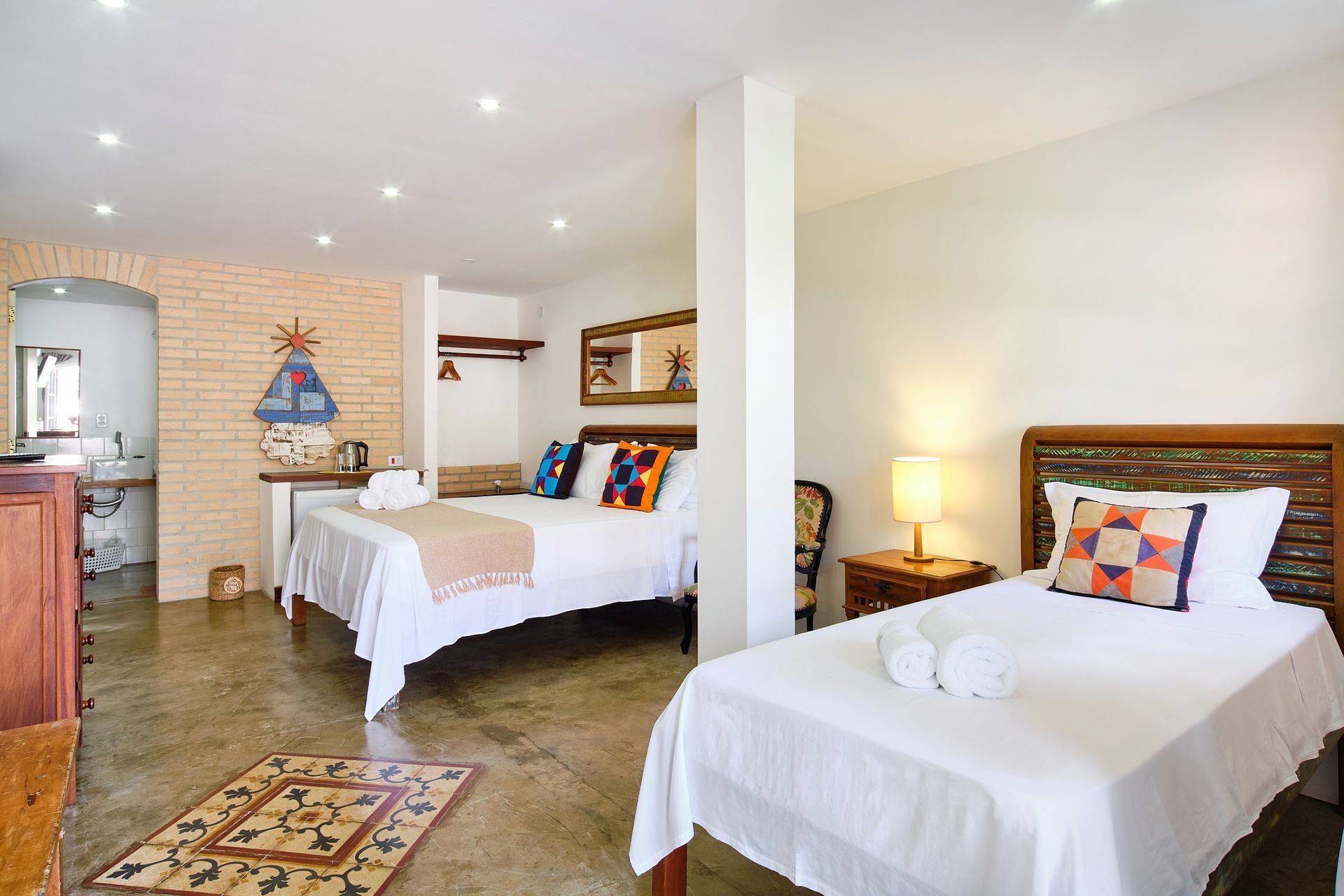 A hotel room featuring two beds, a tiled floor, brick wall accents, and a bathroom visible in the background.