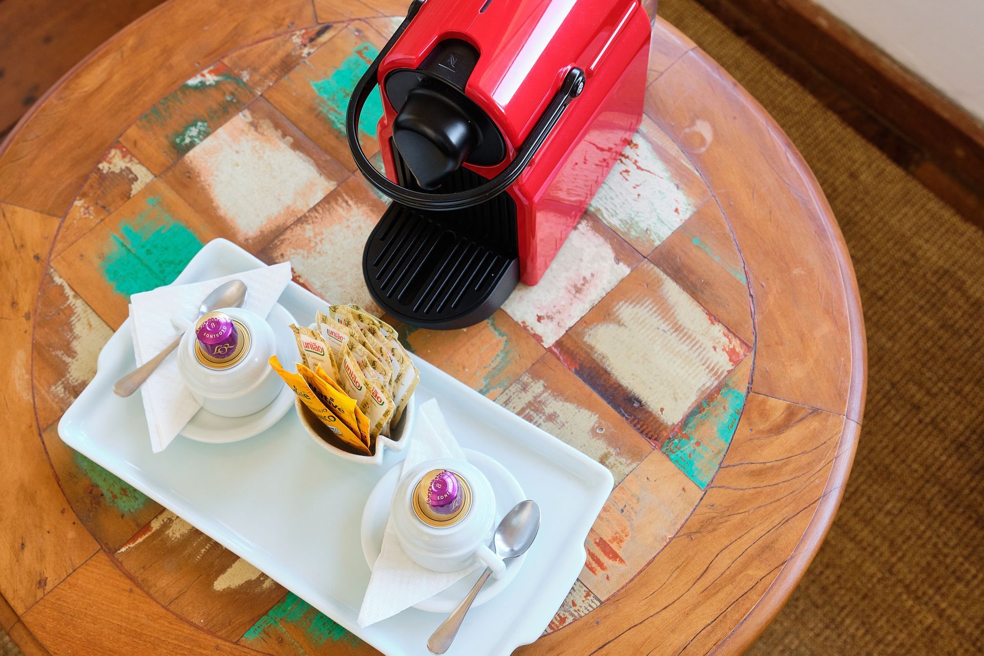 A red Nespresso machine and a white tray with two coffee cups and snacks on a rustic wooden table.