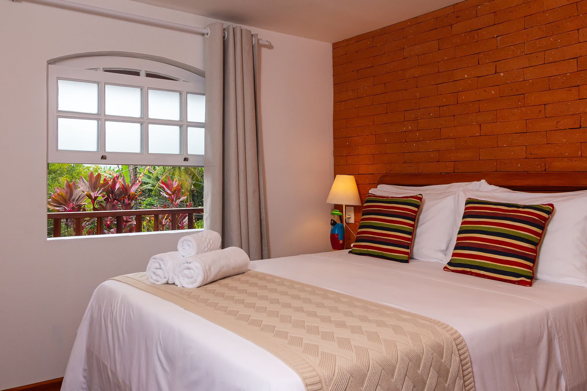 A hotel room with a queen bed featuring white linens, a textured runner, and striped pillows against a brick wall.