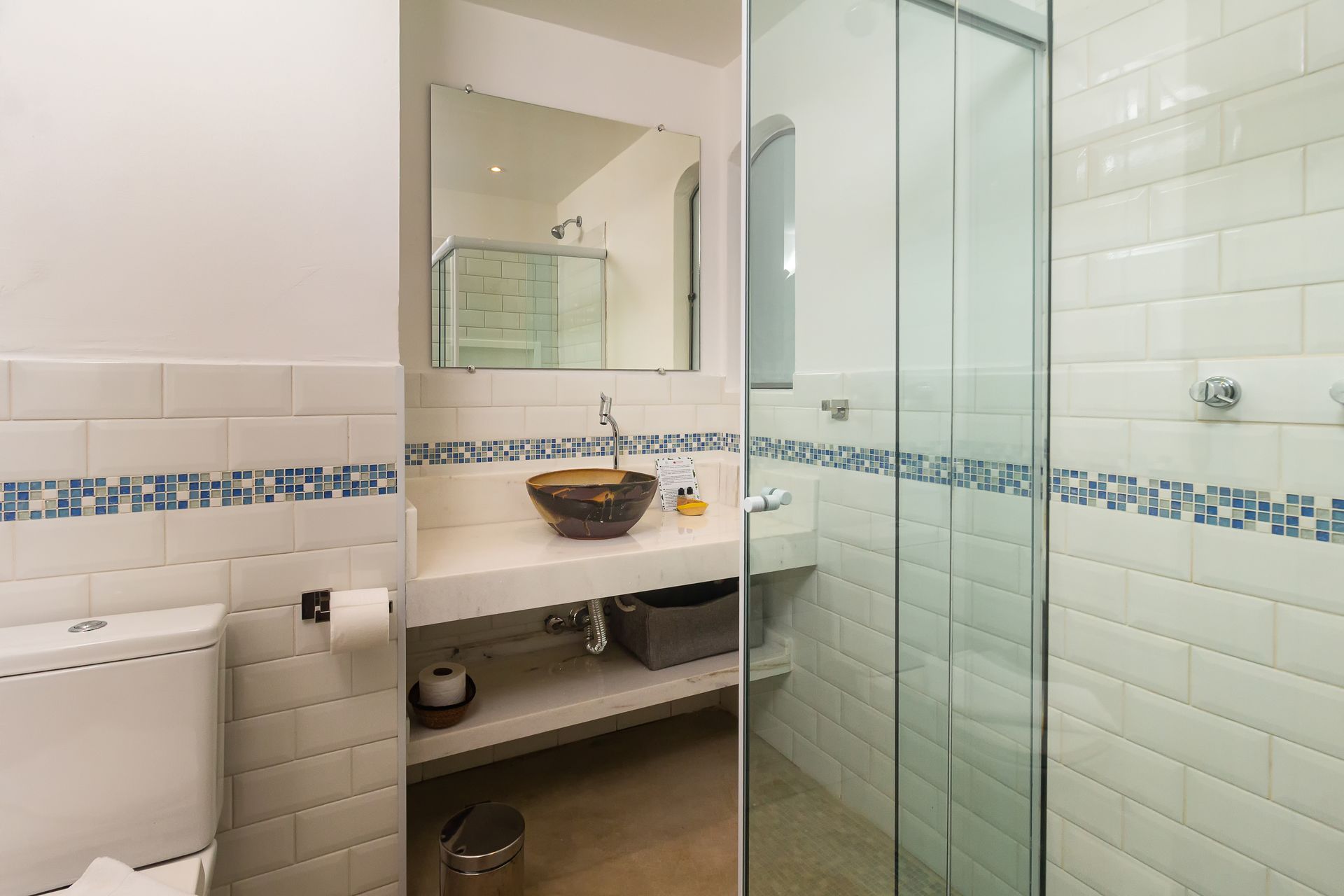 A modern bathroom with white subway tiles, a blue mosaic border, a vessel sink on a vanity, and a glass-enclosed shower.