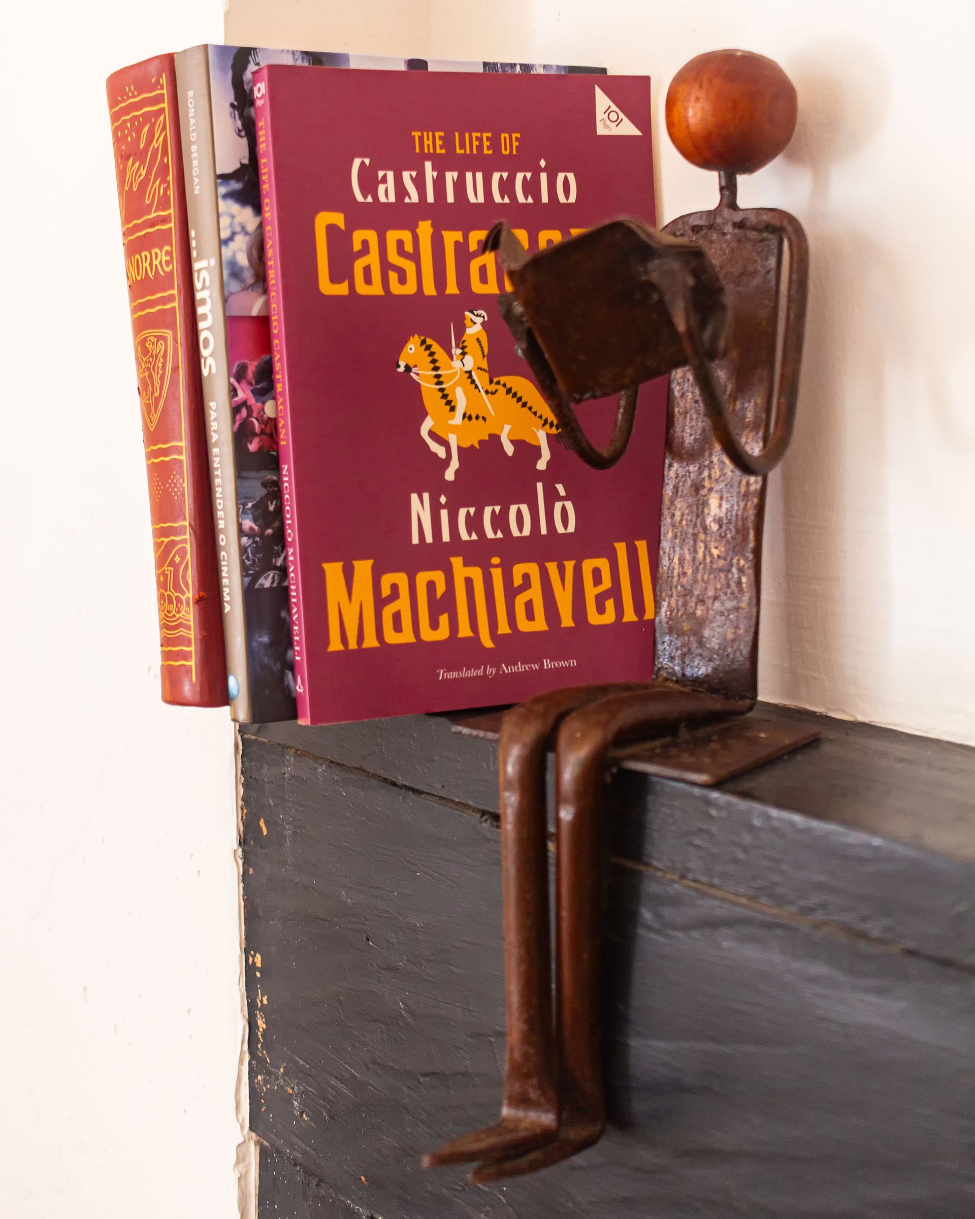 A metal sculpture of a figure sitting on a ledge, reading a copy of Niccolò Machiavelli's 