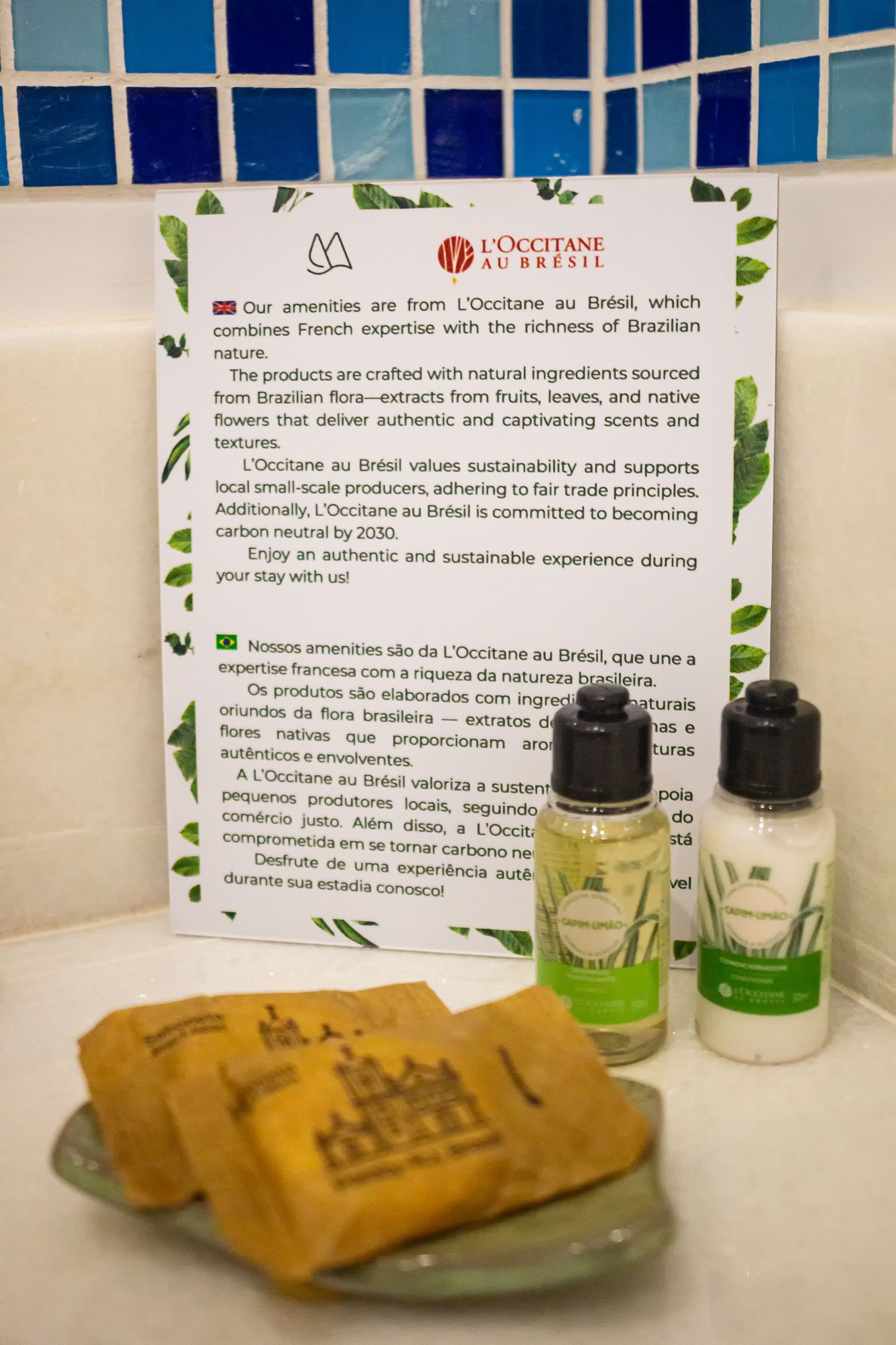 Hotel bathroom amenities including two soap bars, a small shampoo bottle, and a conditioner bottle in front of a sign.