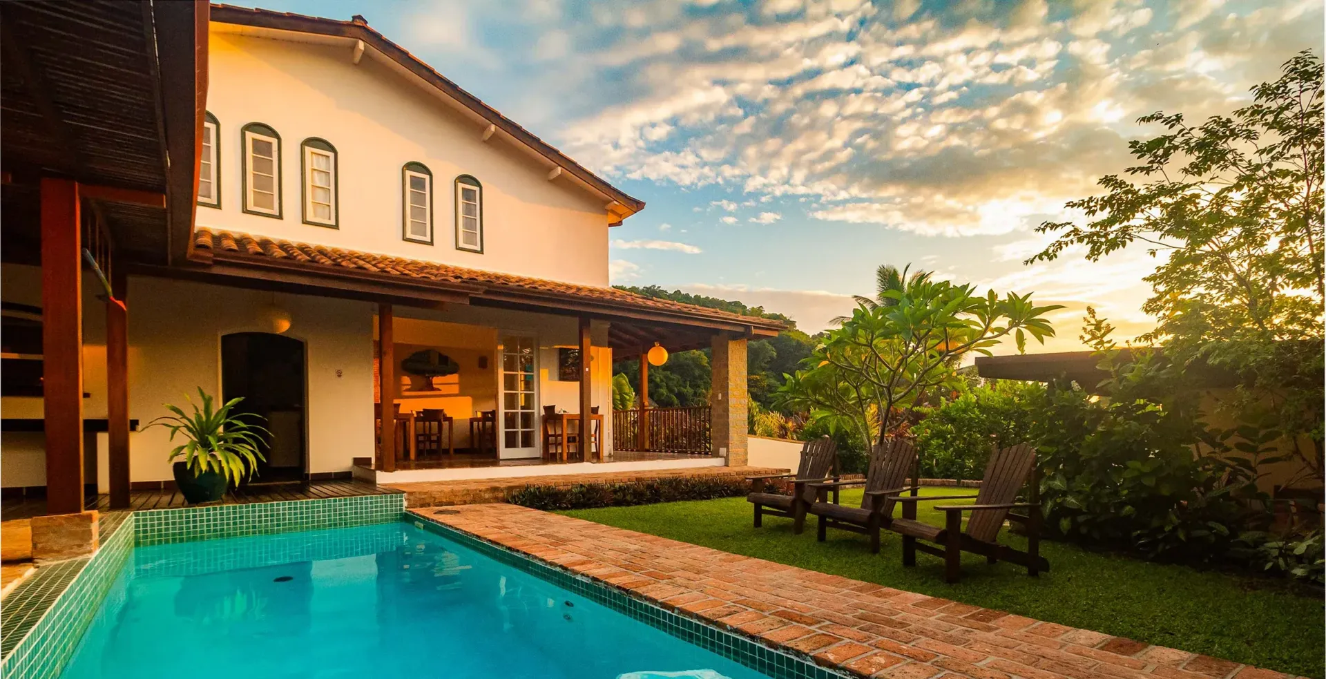 Sunlit villa patio with turquoise pool, covered porch, and garden at sunset