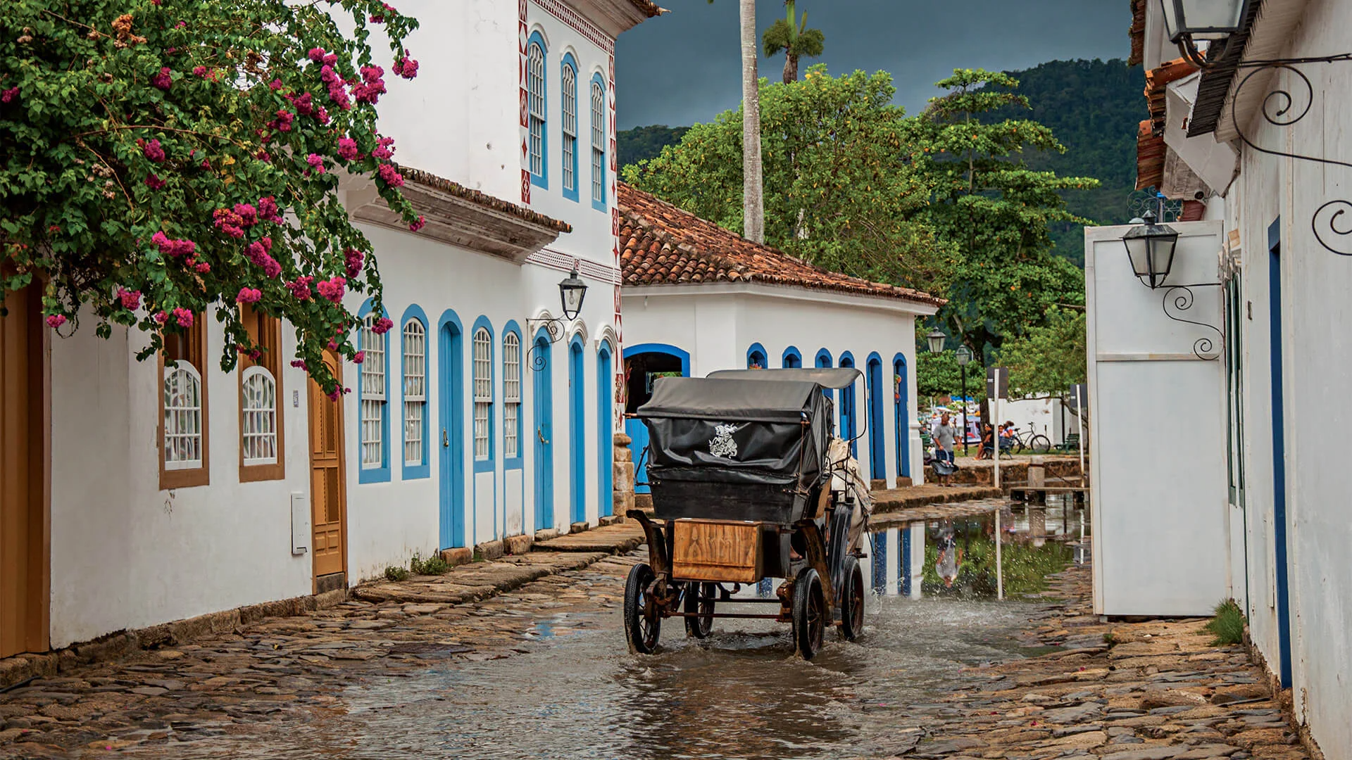 A horse-drawn carriage travels down a cobblestone street lined with white colonial buildings under a stormy sky.