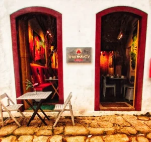 Entrance to Thai Paraty restaurant with two arched doorways, a small outdoor table, and cobblestone ground.