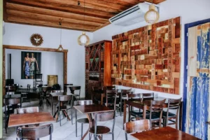 Interior of a restaurant with wooden tables and chairs, a wood-paneled ceiling, and a large decorative wall sculpture.