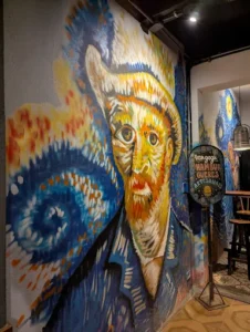 A large wall mural featuring a stylized portrait of Vincent van Gogh in expressive brushstrokes, set inside a shop.