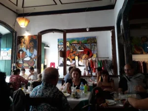 People dine in a restaurant featuring large, colorful wall paintings of musicians and traditional scenes.