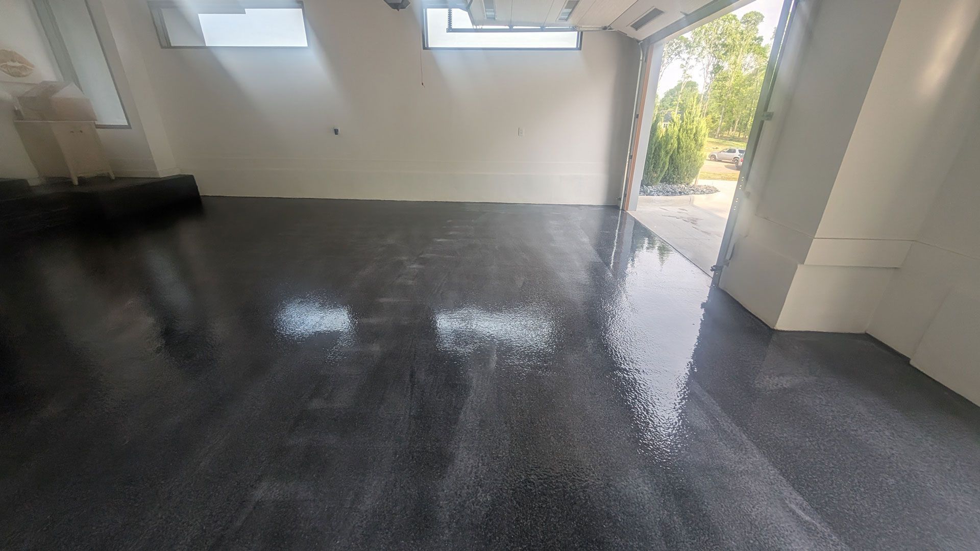 Shiny wet gray floor in a garage with sunlight coming through open doors and windows